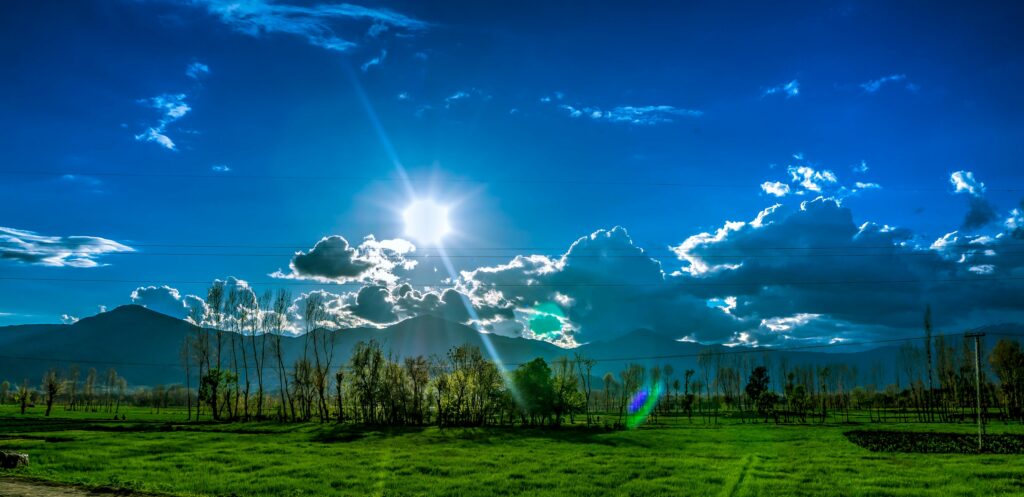 Scenic view of Kalam's green fields and dramatic sky under bright sunlight.